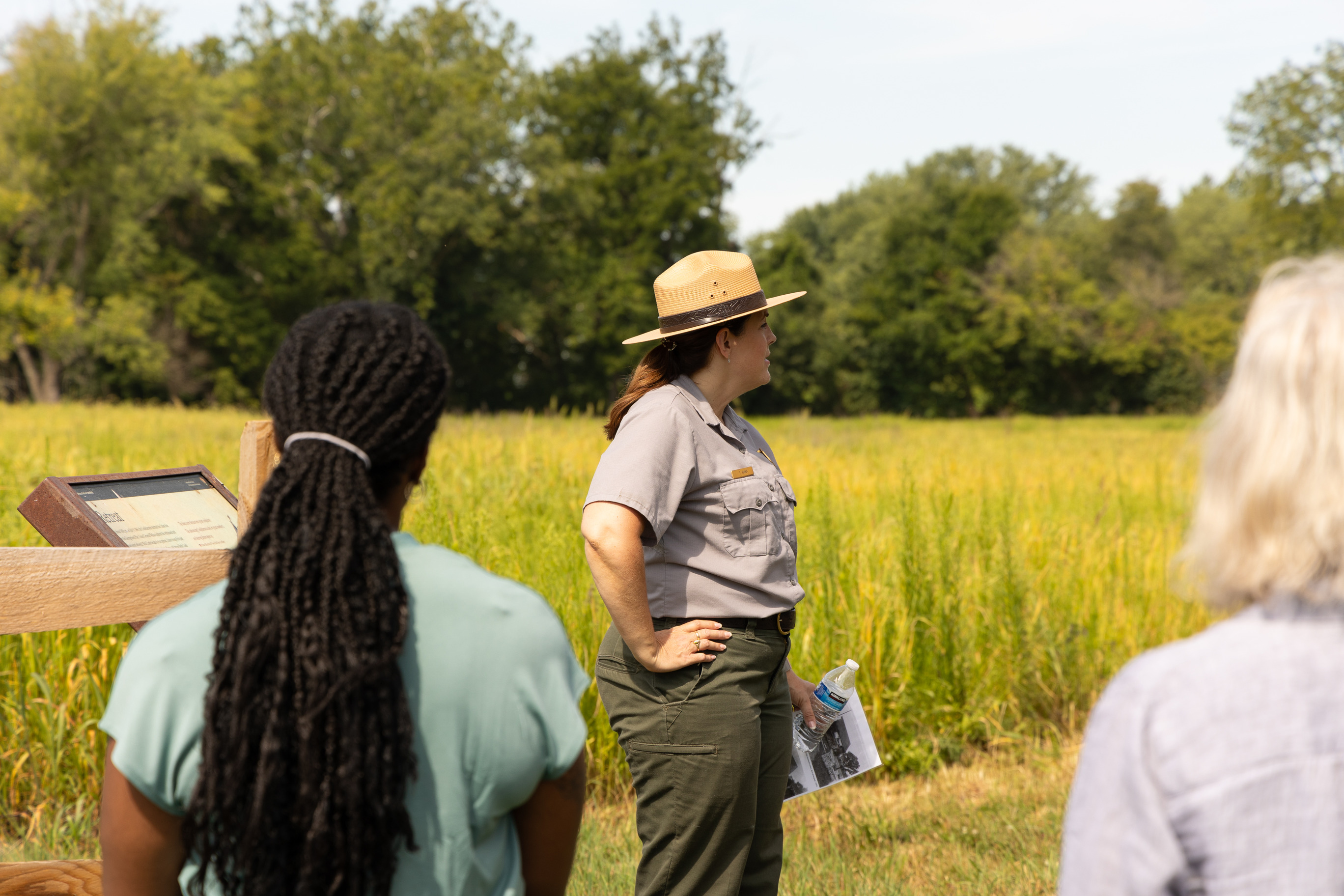 A park ranger stand in front of visitors in front of a grassy field on a trail. 