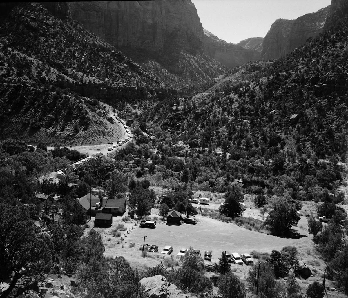 Oak Creek bridge and view of canyon- group of 75 motorhomes in caravan called the Fireballers, preparing to drive through tunnel. Park administration buildings in foreground.