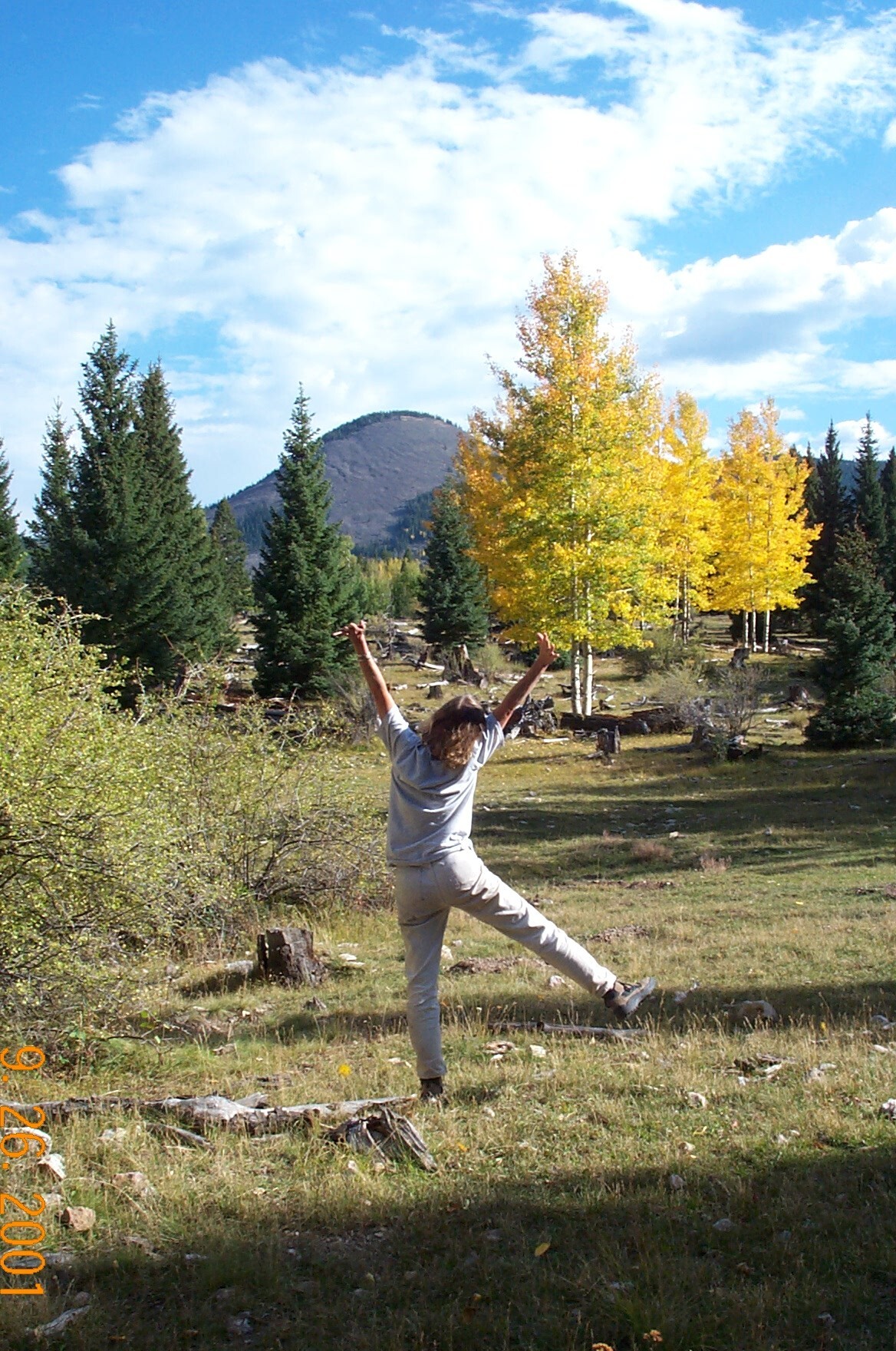 A woman poses in excitement with golden aspens and a talus mountain slope in the distance.