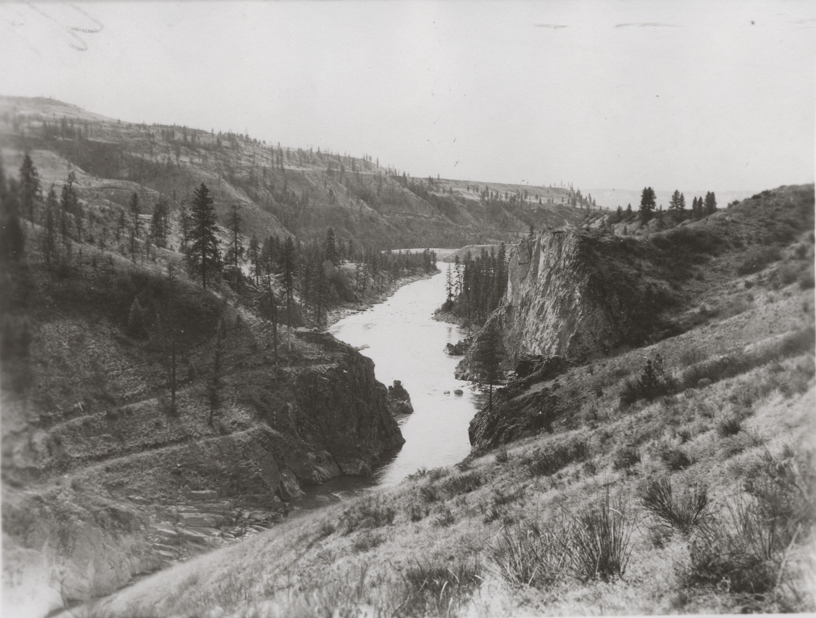 Black and white photograph of a river in a steep sided valley with partially forested hills