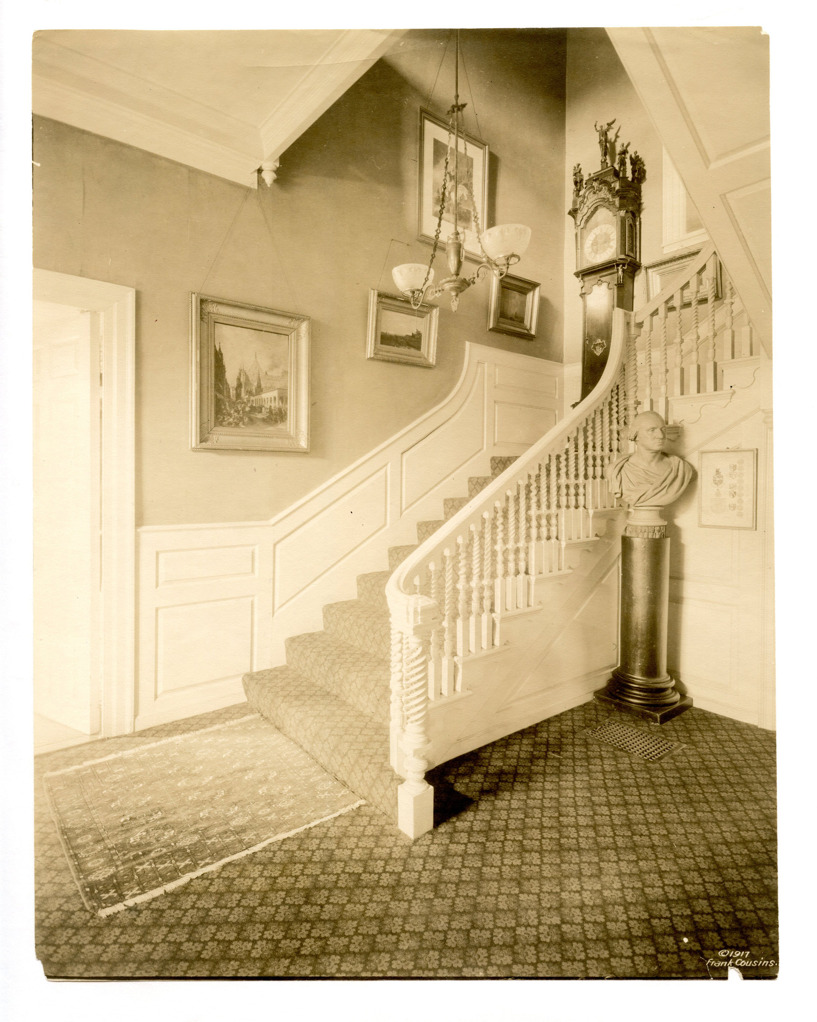 White staircase decorated with paintings, a chandelier and a bust of George Washington.