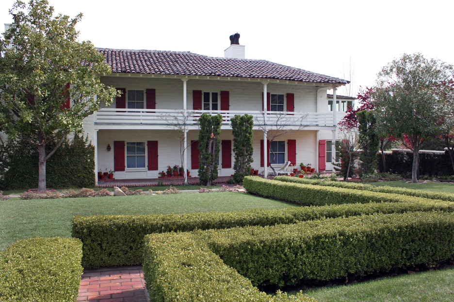 The Eugene O'Neill Tao House courtyard with a two-story porch and green, trimmed shrubs that form a barrier next to the walking path. 