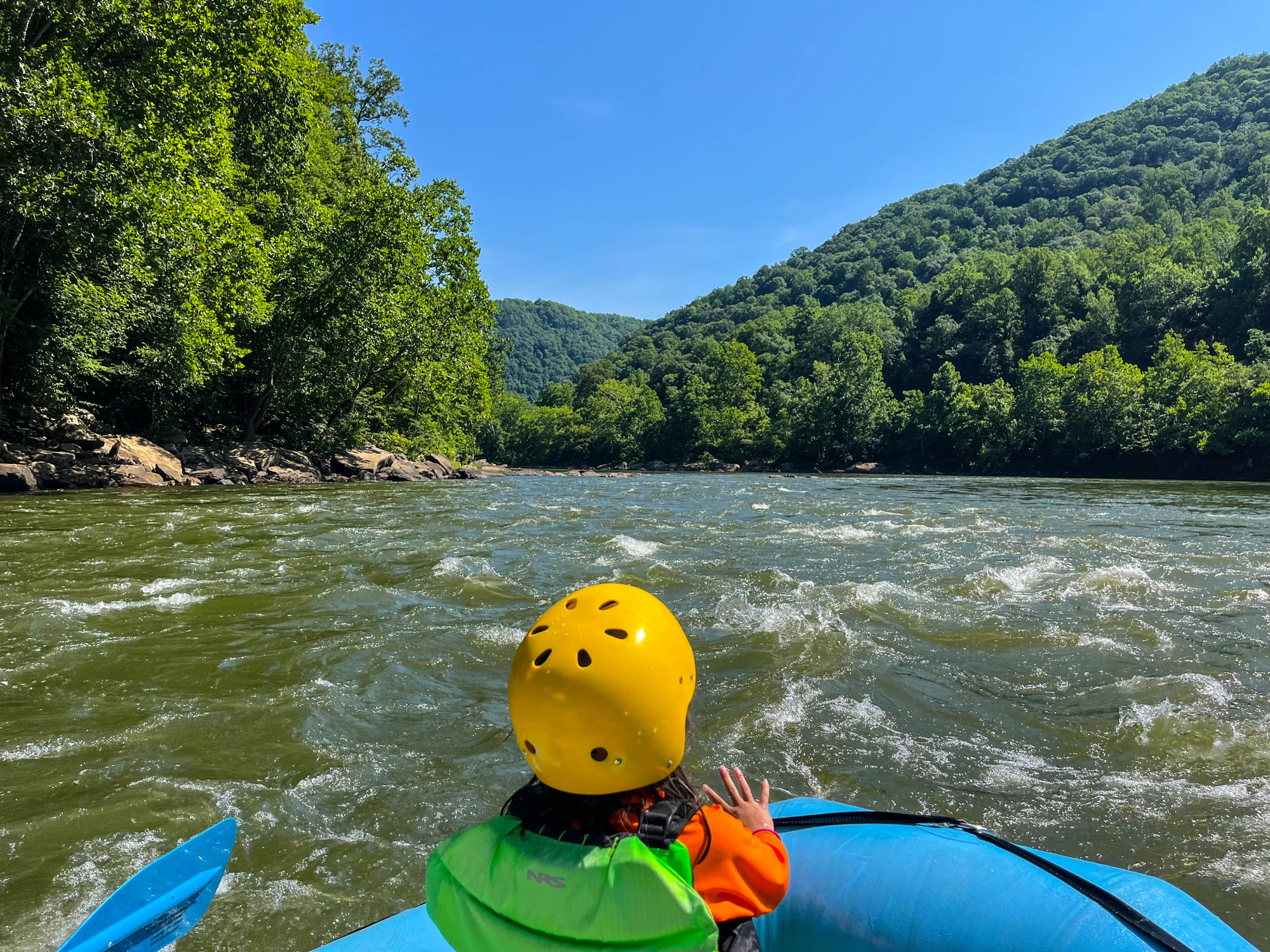 Kids riding a raft on a river lined with trees