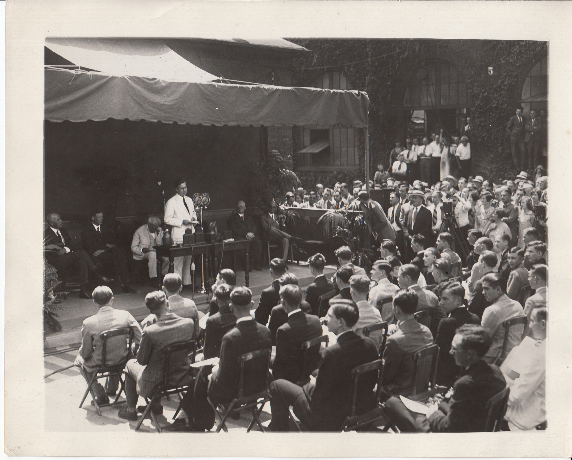 Charles Edison addressing the scholarship contestants in the Laboratory courtyard, Thomas Edison and the other judges seated behind him.