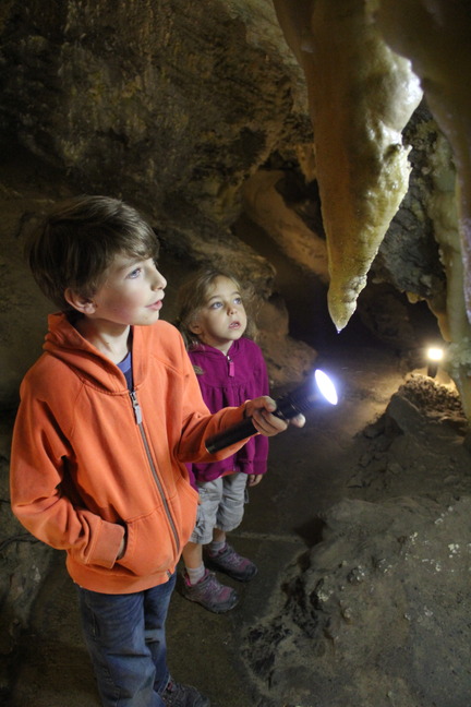 A young boy holds a flashlight and points out a stalactite to a young girl.