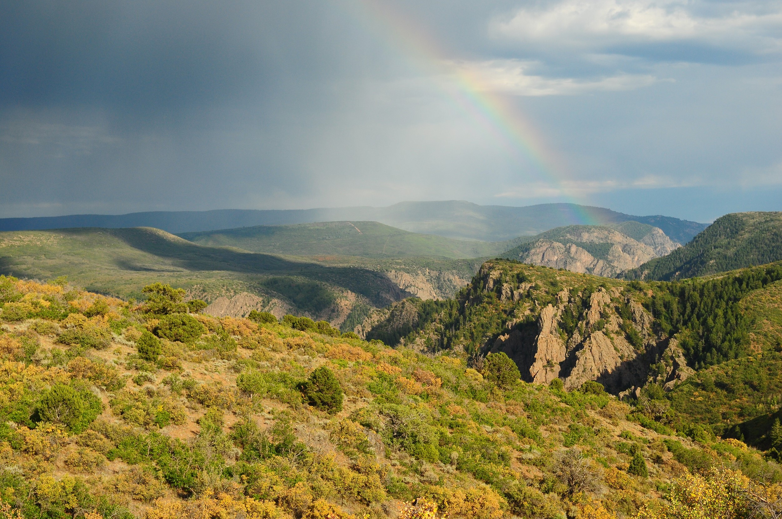 A rainbow over small mountains and a canyon rim