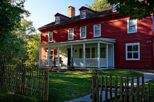 A red house with white trim and a white porch with a wooden fence in the foreground.