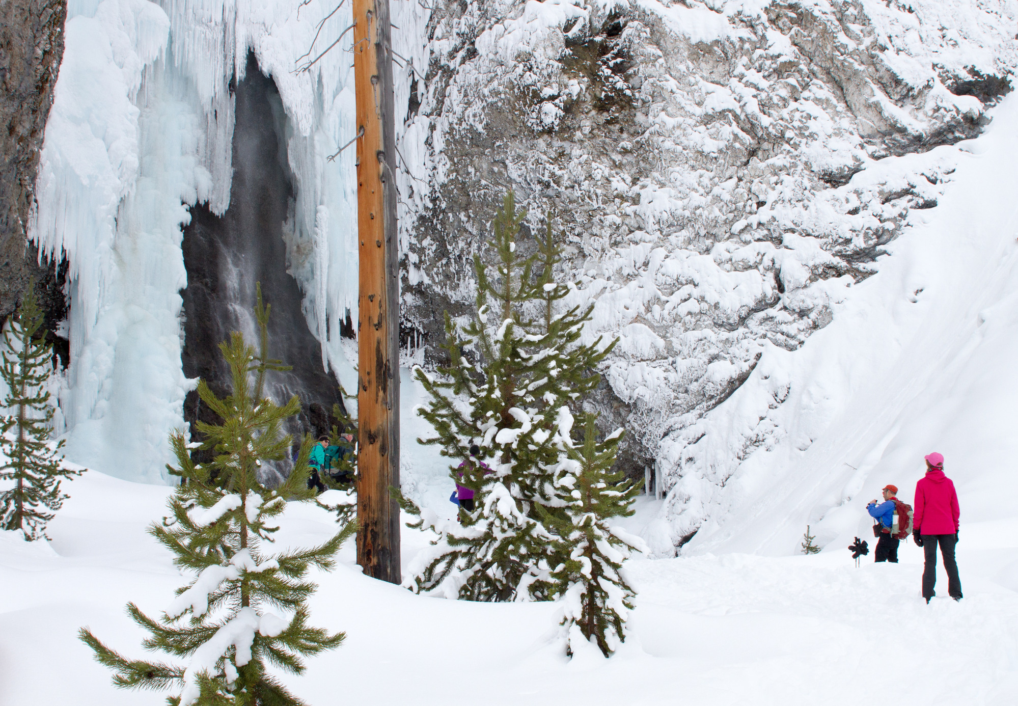 Cross-country skiers stopped below a high waterfall looking at it.