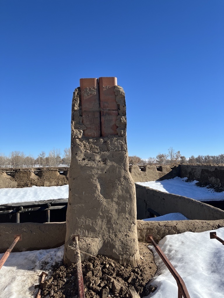 Two layers of amended adobe bricks and an outer coat of adobe have fallen from the kitchen chimney, exposing the interior masonry liner. 