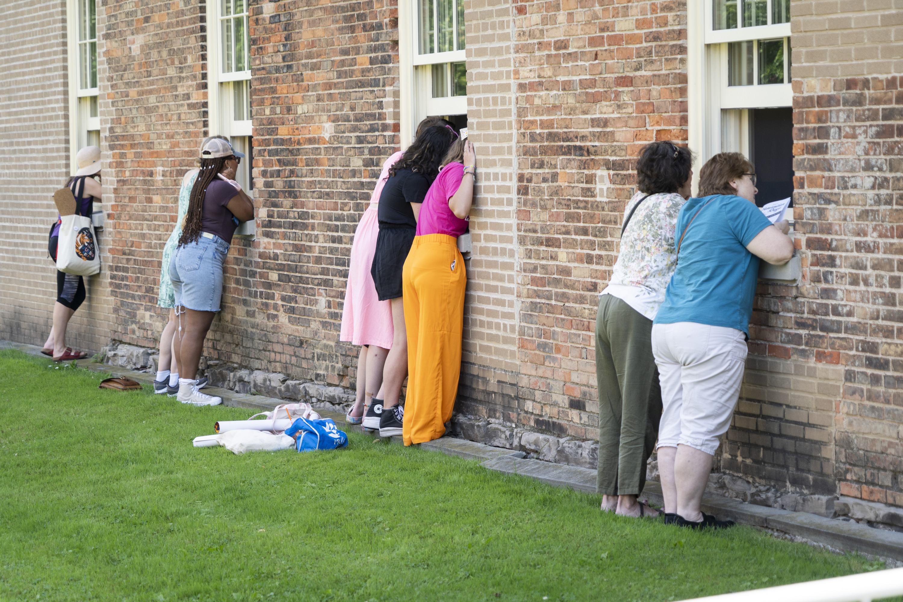 Women stand at open windows on the exterior of a brick building.