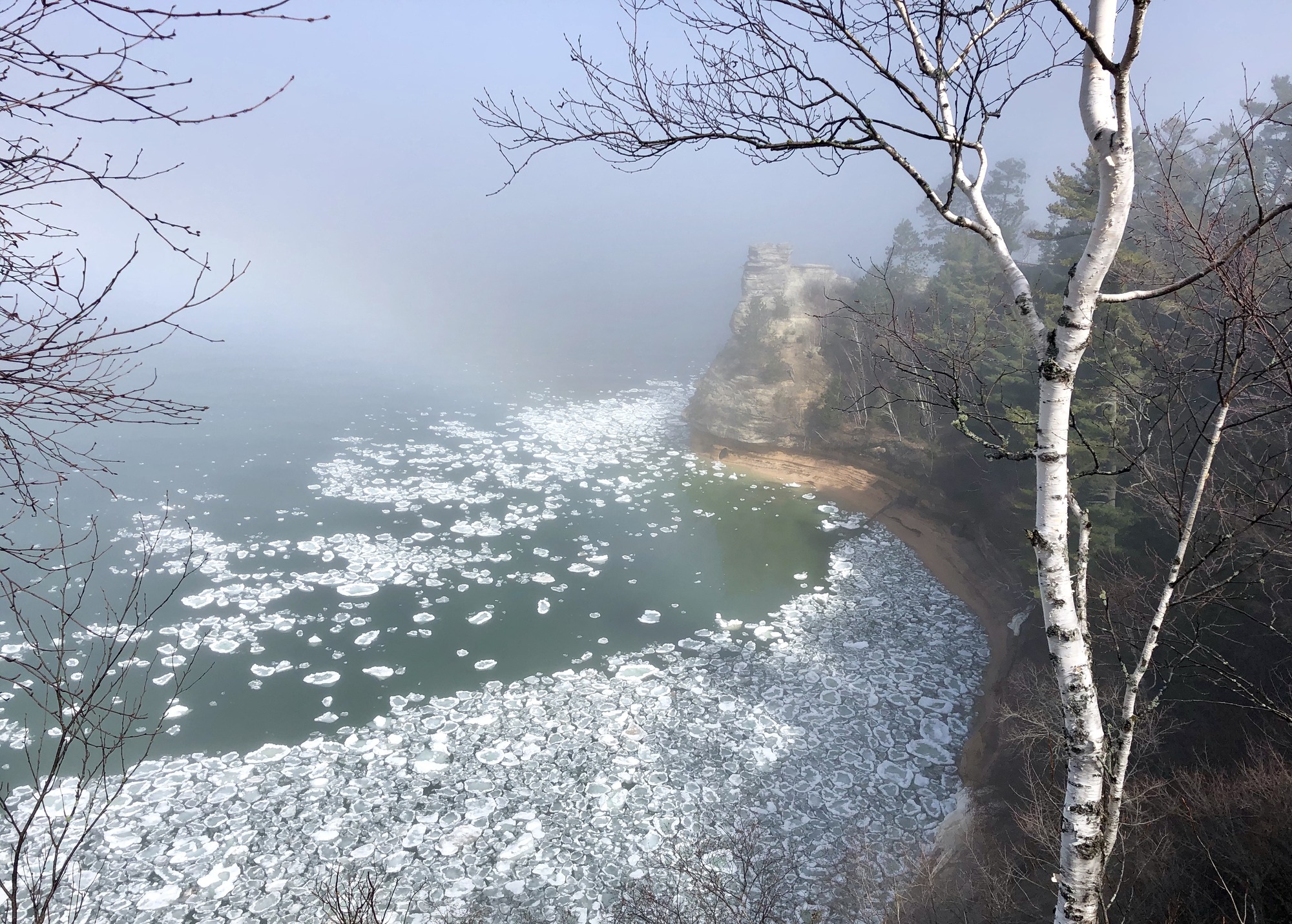Miners Castle rock formation with pancake shaped ice blocks floating in Lake Superior. A faint rainbow in the fog.