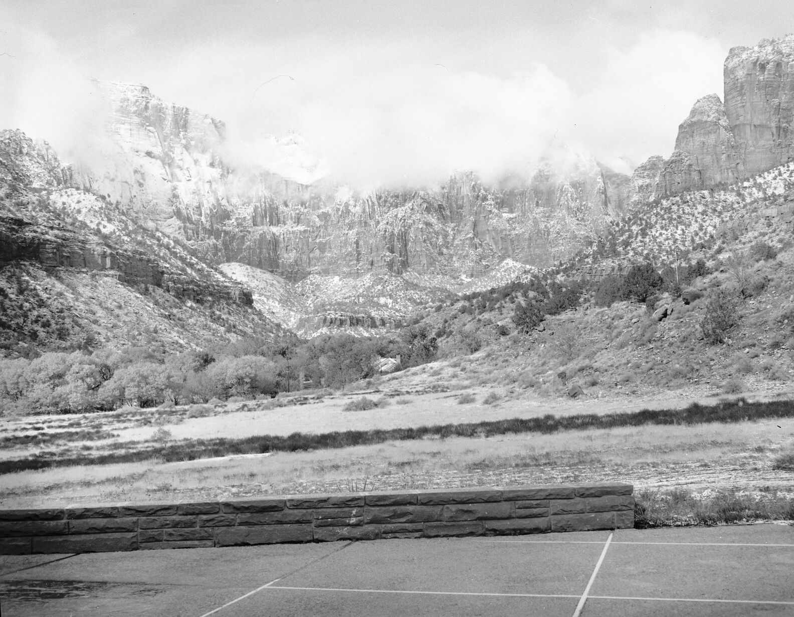 The West Temple and Towers of the Virgin shrouded in clouds and snow, from patio behind the Mission 66 Visitor Center and Museum and headquarters building.
