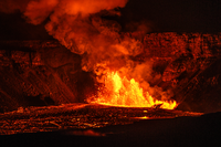 Fountains of lava shoot hundreds of feet in the air at night from within a crater. 