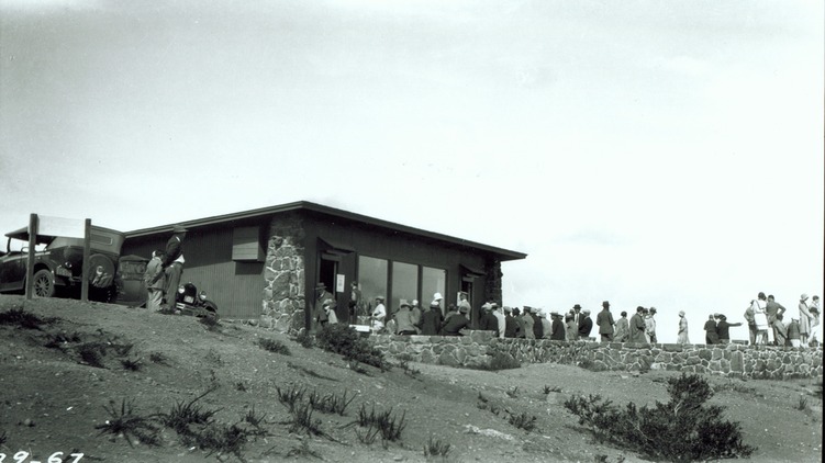 Black and white photograph from 1967 that shows a group of people standing at an overlook in front of a square building. 