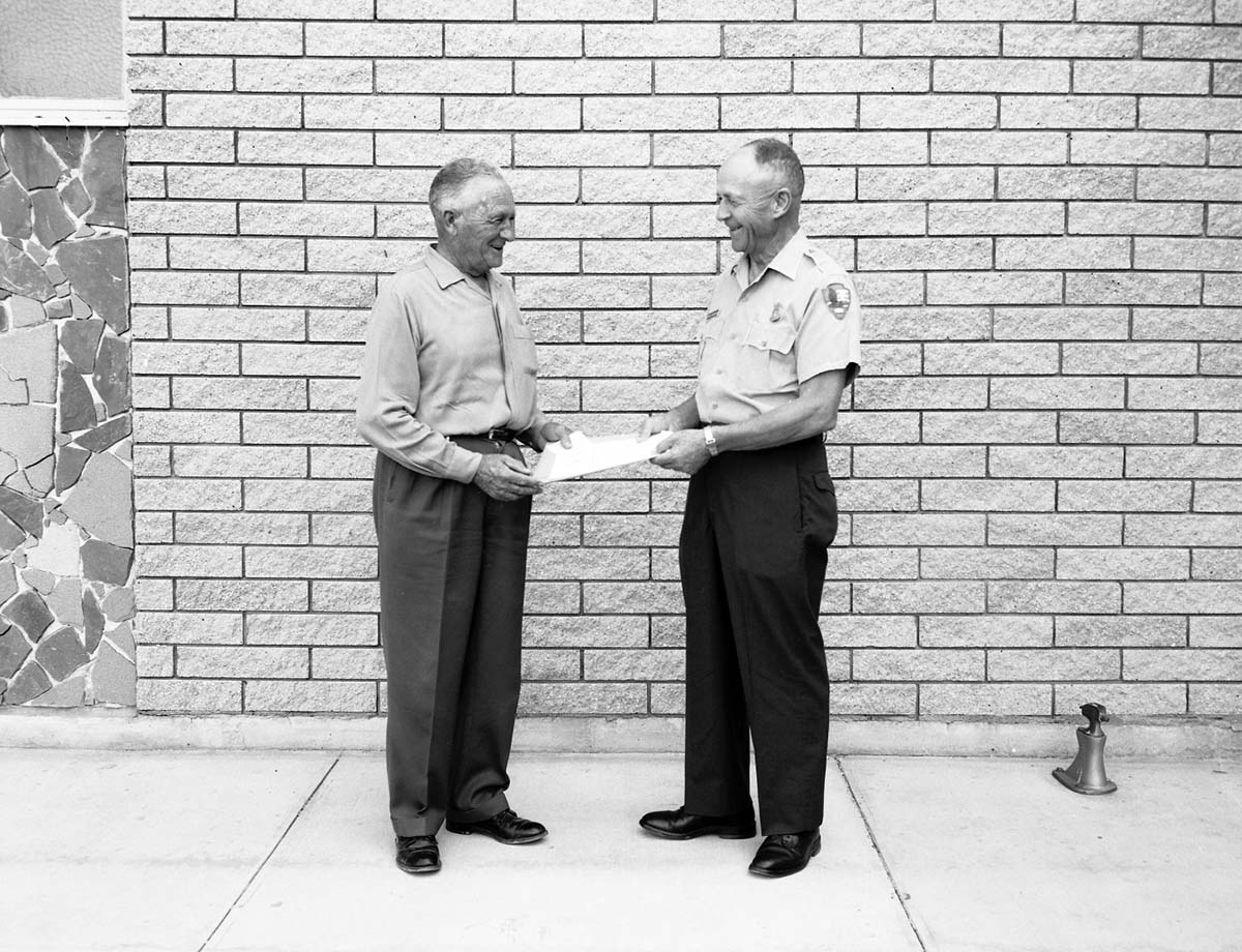 Superintendent Oberhansley presenting award for meritorious service to Dewey Excell upon his retirement, in front of Mission 66 Visitor Center and Museum.