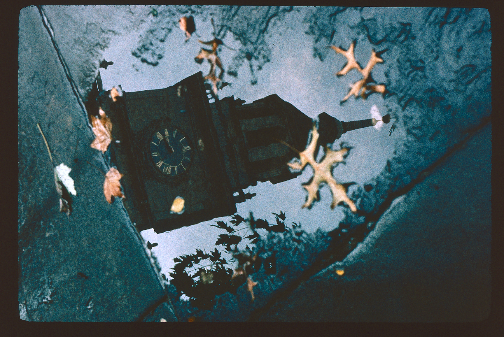 Independence Hall. Exterior. Independence Hall tower reflected in a puddle on the pavement with autumn leaves on top. Tower clock, 3:15 PM.