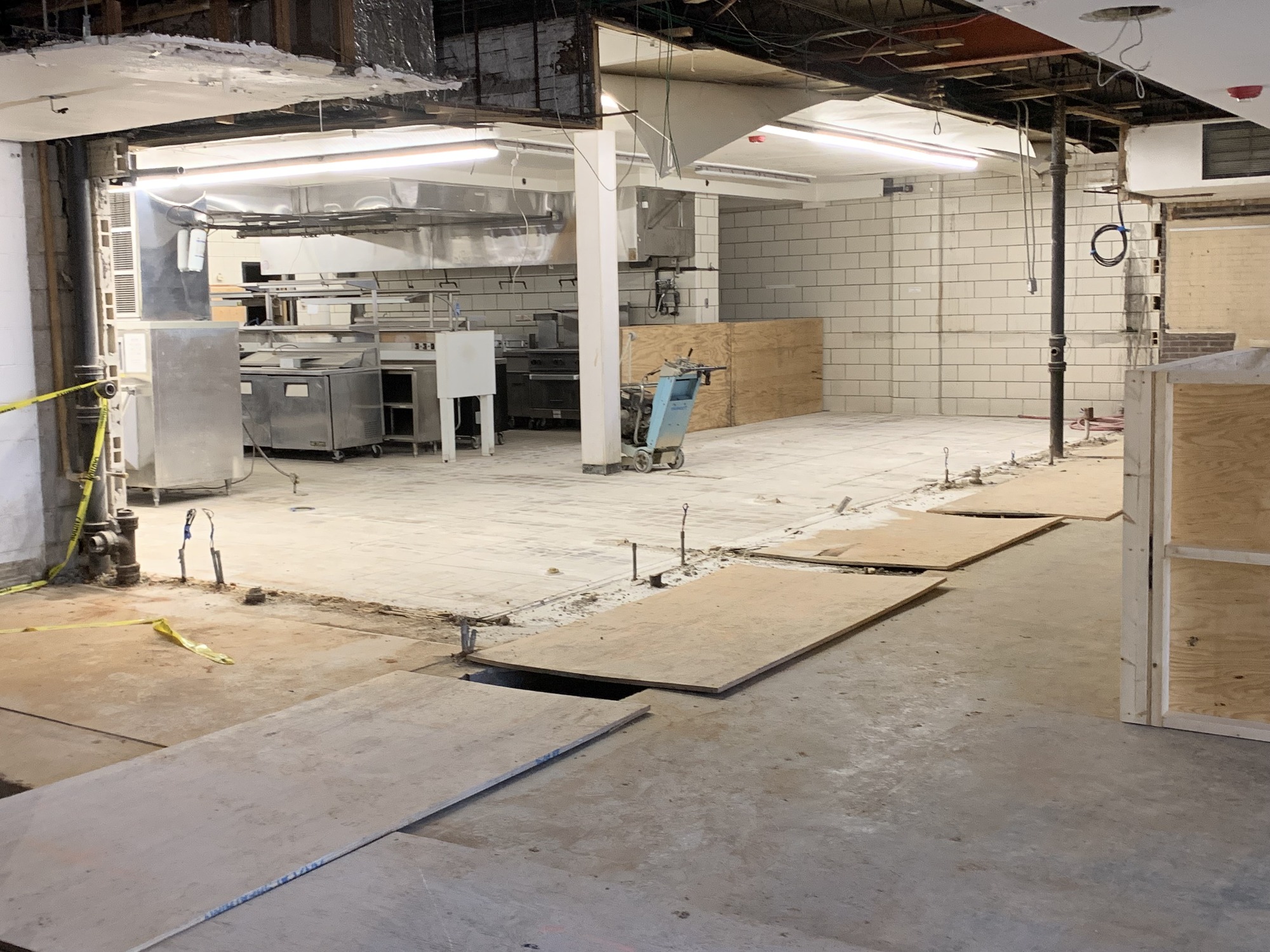 A large room under construction with wires sticking out of the concrete floor and plywood boards laying around.