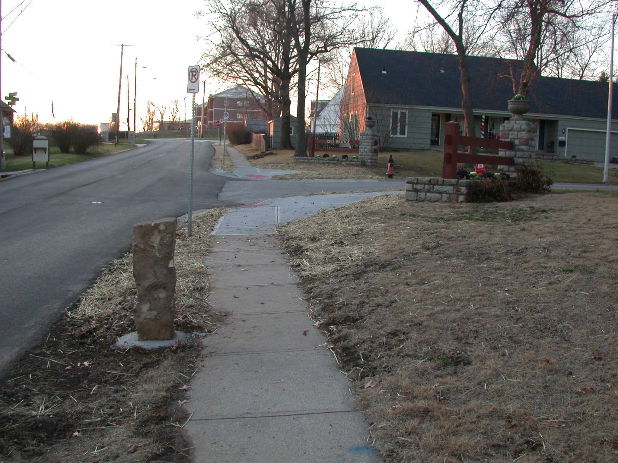 A sidewalk next to a house with trees around it.