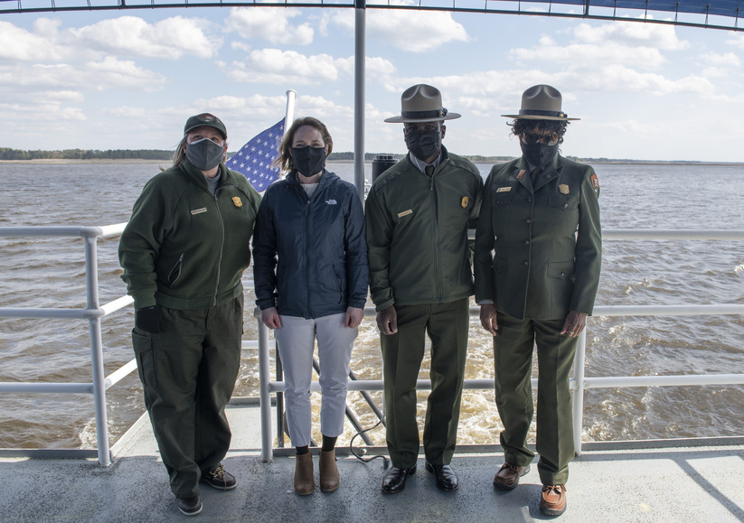 Four federal officials stand on the deck of a boat.