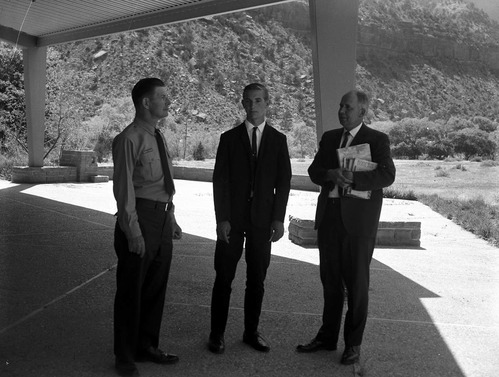 Creed Fraehner stands between Superintendent Warren F. Hamilton and Jim Clarke on the patio of the Mission 66 Visitor Center and Museum. Clarke is holding books awarded to Fraehner for winning the National Park Service 50th Anniversary poster contest.