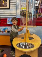 A small child at a clear tube, holding a parachute inside. 