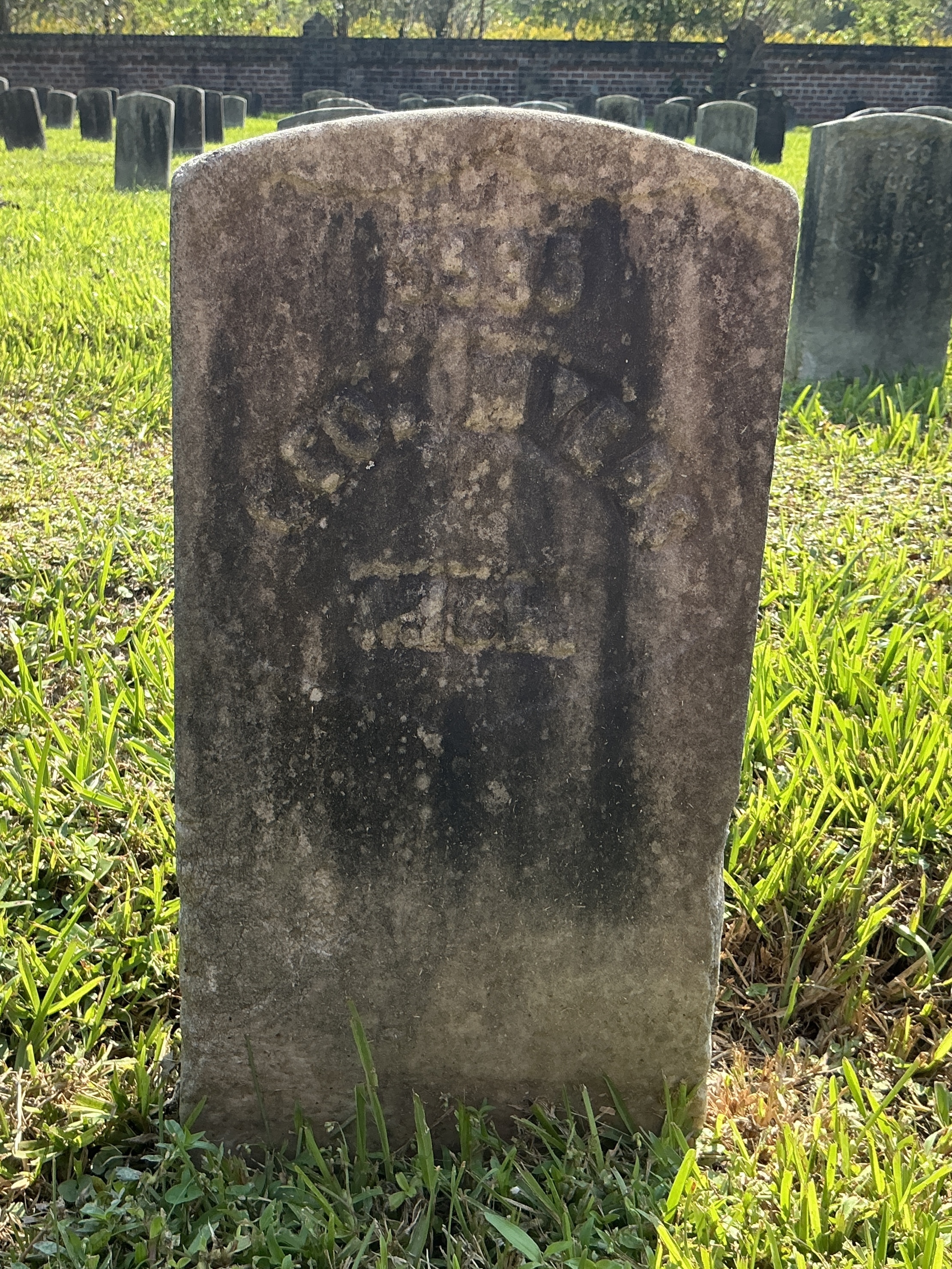 Front of historic upright marble headstone with recessed shield with recessed lettering face.