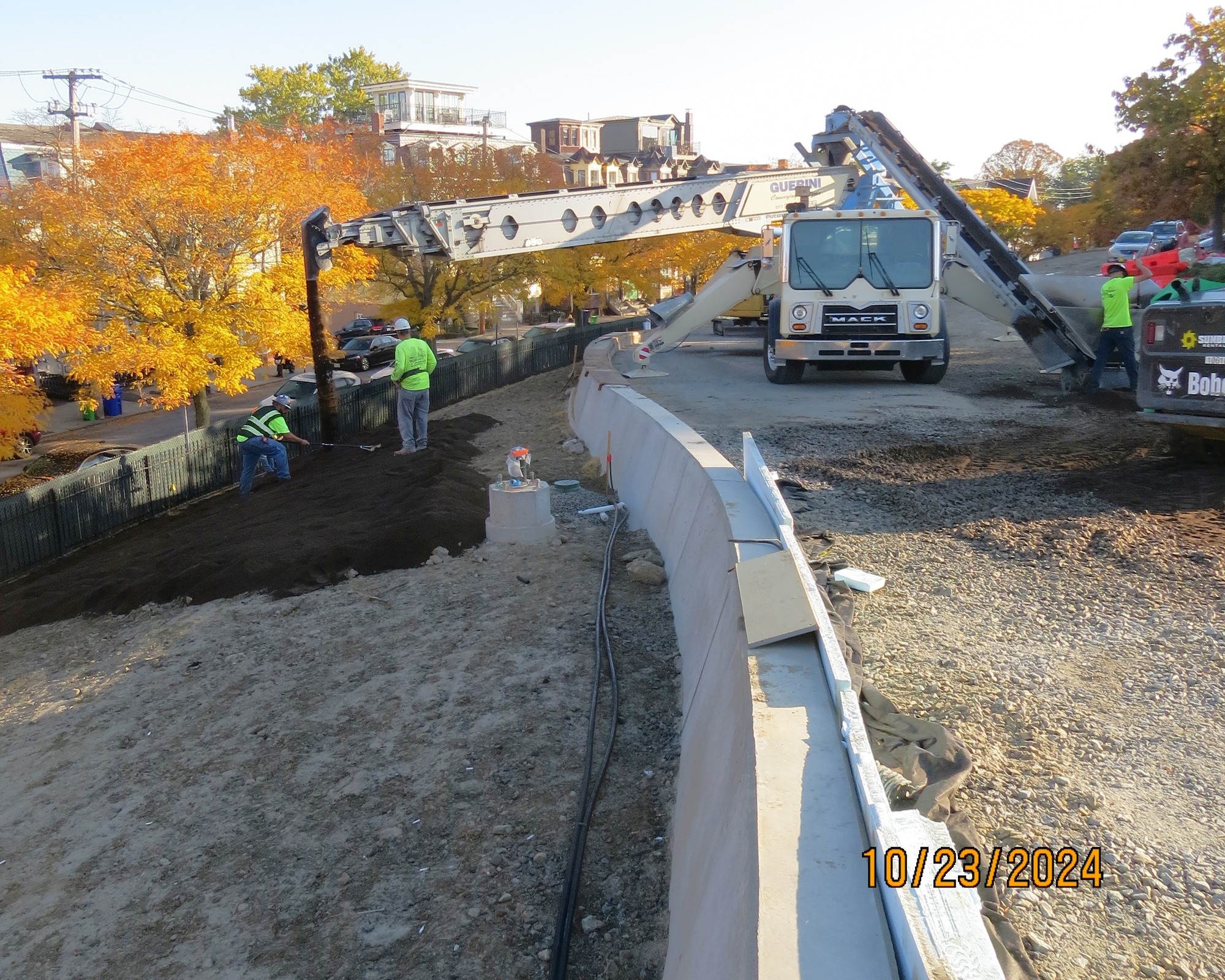 A truck with a conveyor belt dropping dirt across a side of a hill. Workers move the dirt around. 