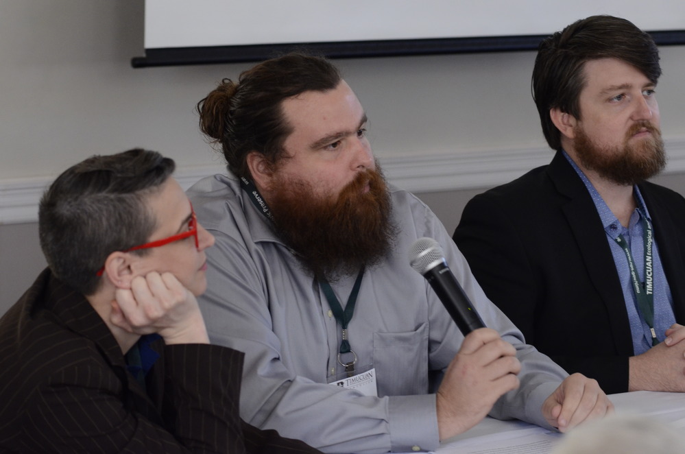 three people seated behind a table, one holds a microphone