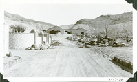 This is an historic black and white photograph from the Scotty's Castle Historic Photograph Collection, Death Valley National Park looking east down road to Scotty's Castle Stables. Retaining Wall on left. Watercourse on right. January 17, 1931. Photographed by Mat Roy Thompson.
