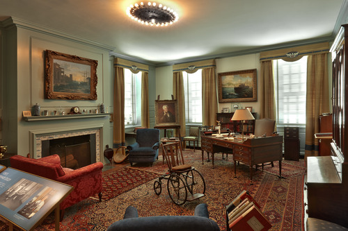 A cozy room furnished with a desk, comfortable chairs, and FDR's wheelchair in the center of the room.