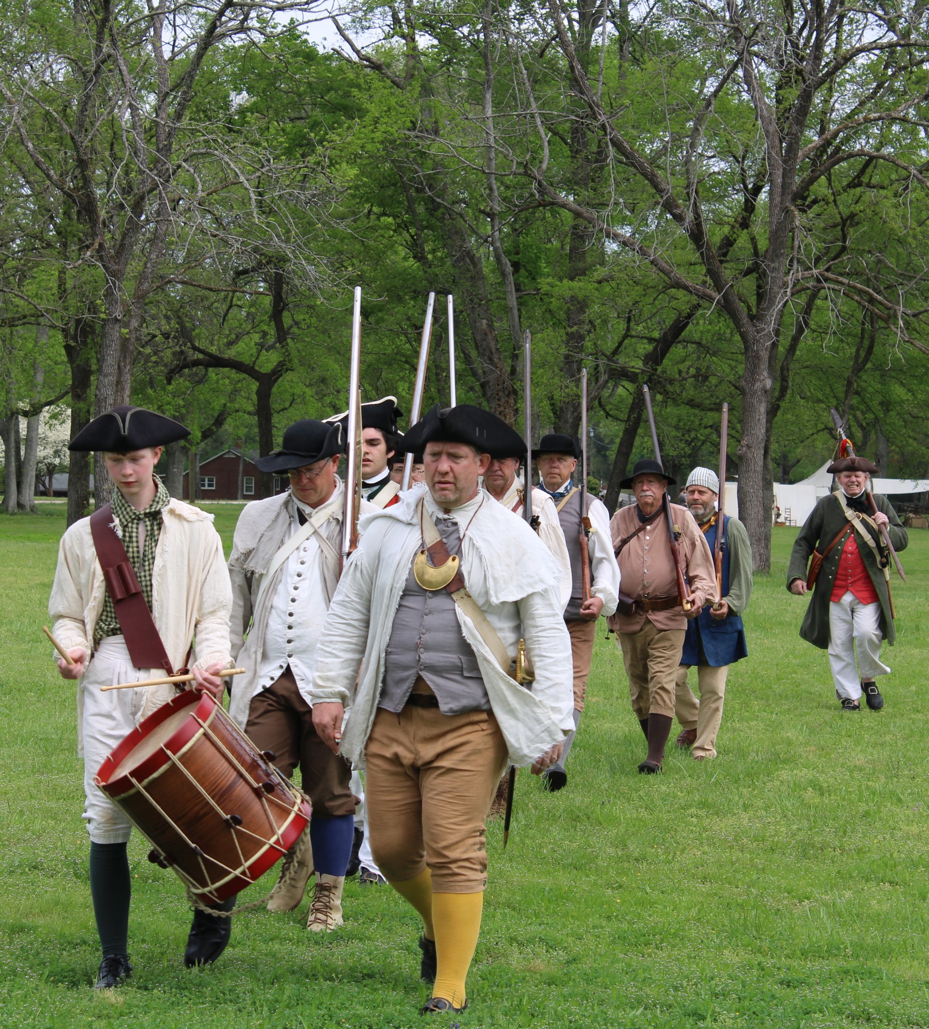 Men in colonial clothing with muskets lead by a drummer.