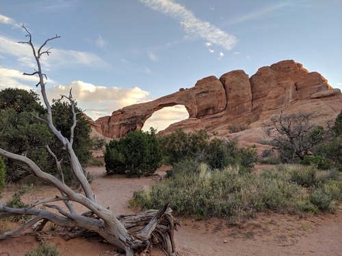 a stone arch sloped downward to the left with bright clouds above it