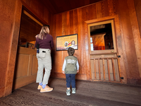 A parent and two children look at an indoor exhibit with text and photos. 