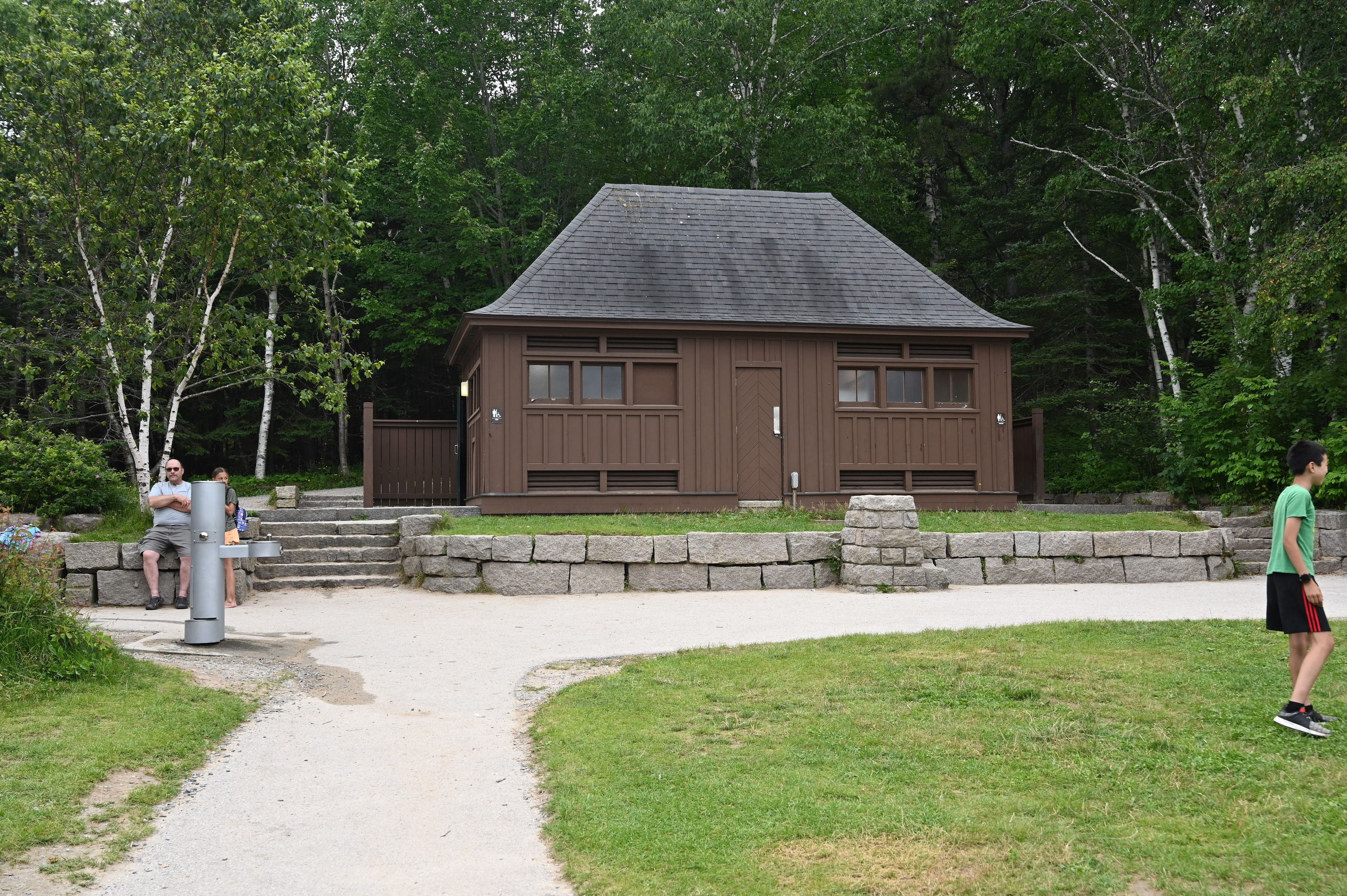 Brown building sitting atop short grassy area lined with grey stones. 