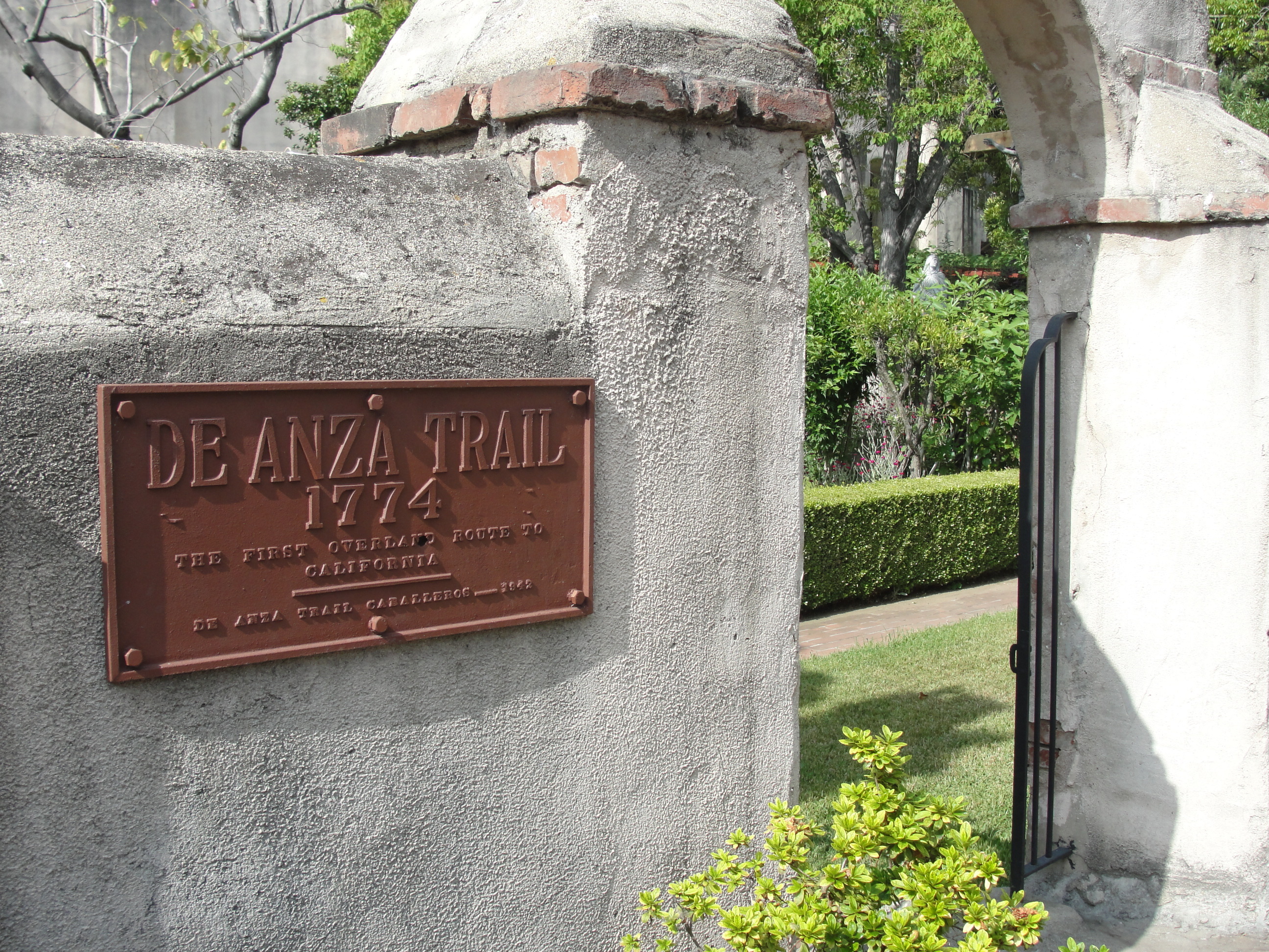A gated concrete archway with a brown plaque De Anza Trail 1774