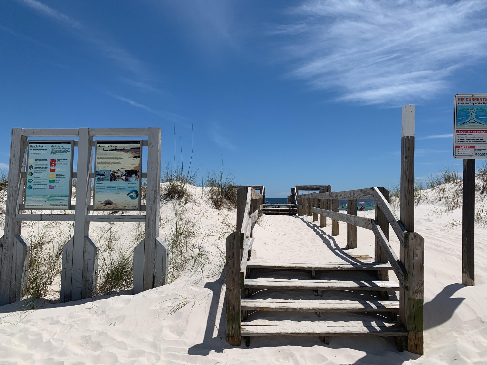 Wooden steps and boardwalk over white sand leading to blue water and blue sky in the background. Two wooden framed National Park Service signs to the left.