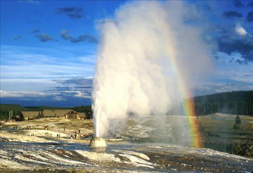 Beehive Geyser with rainbow, visitors, and Old Faithful Lodge in background
