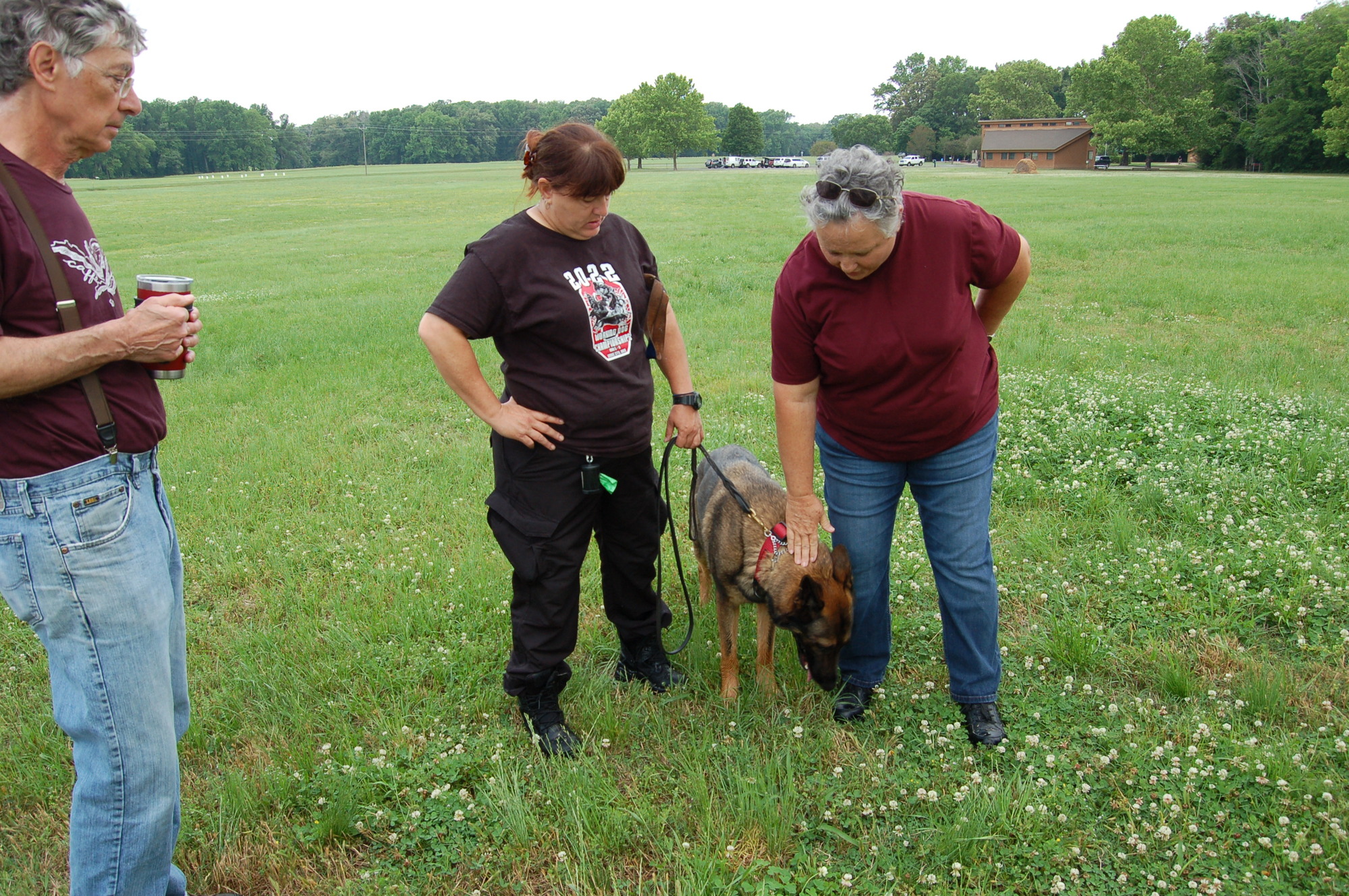 A group of people standing next to a dog on a leash and petting it.