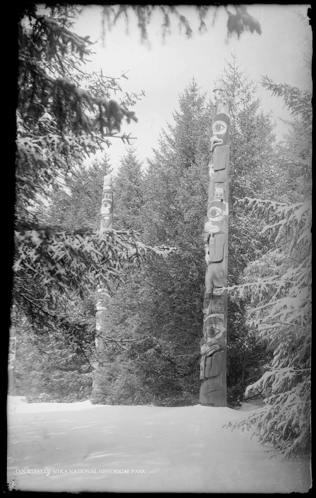 Multiple totem poles in the forest along a curved trail.