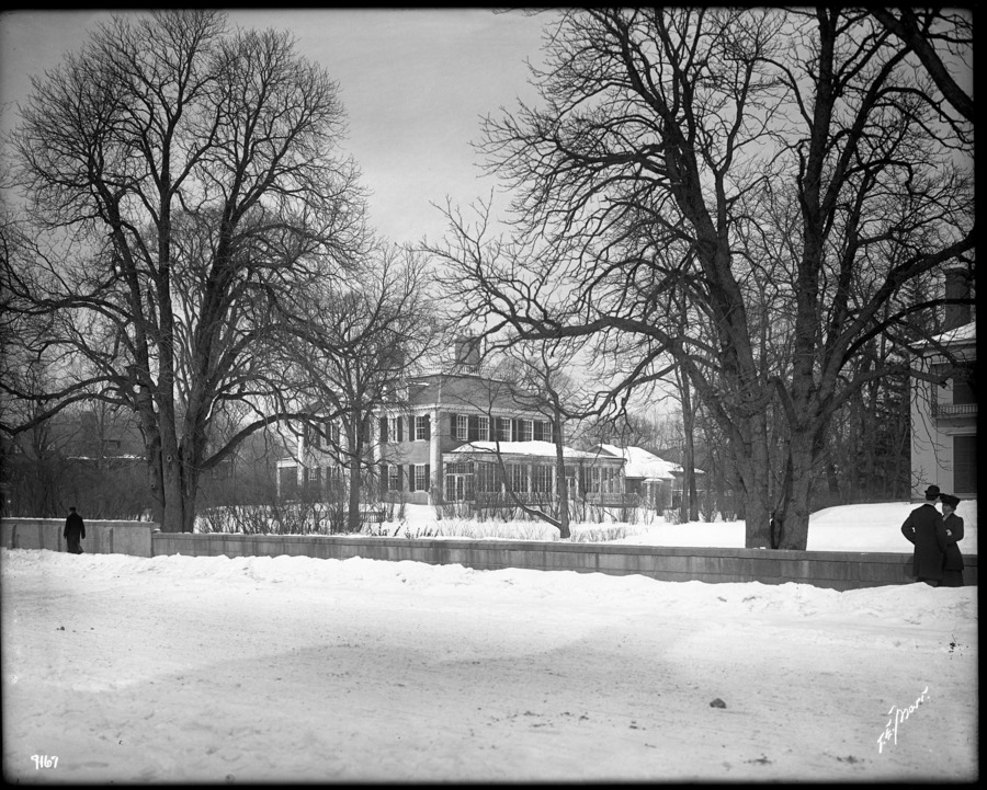 Several people pass through snowy side walks in front of Georgian mansion.