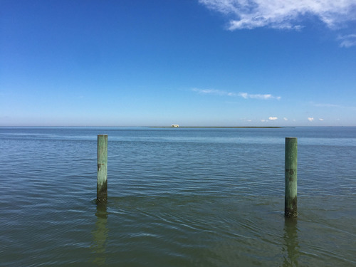 Wooden poles standing in the ocean with a house on an island in the distance