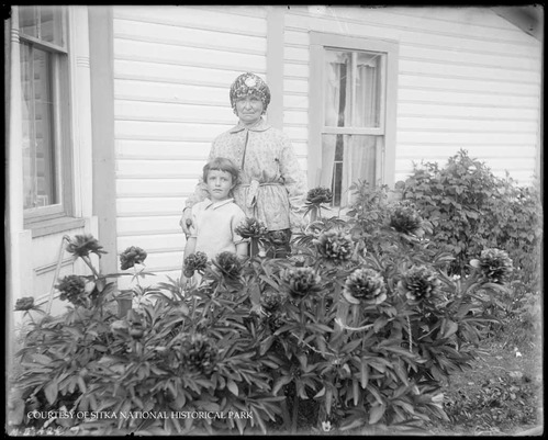 Woman and child behind a row of flowers next to a house.