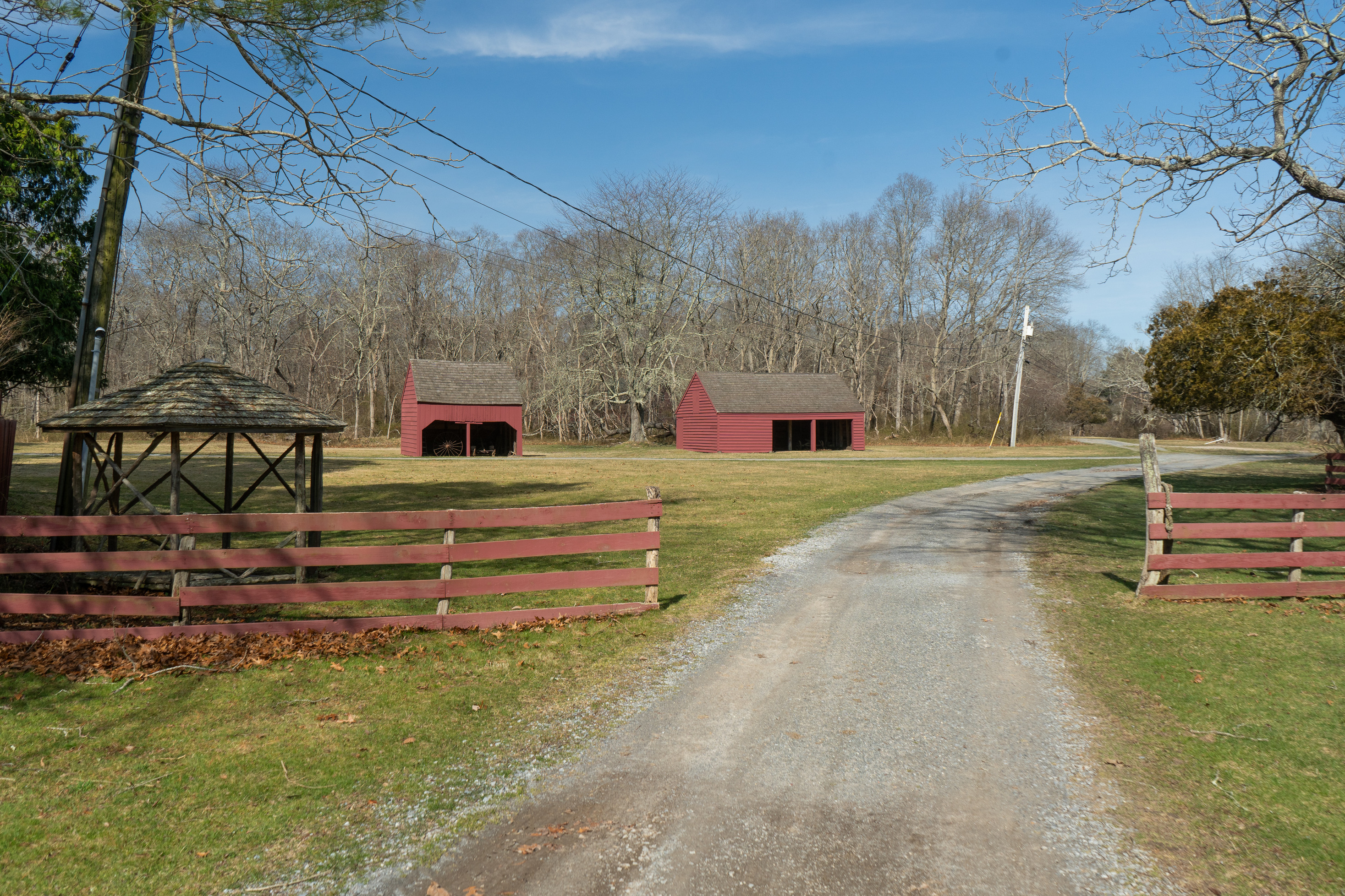 Two red barns in a grassy area with a wooden gazebo and red fence in the foreground.