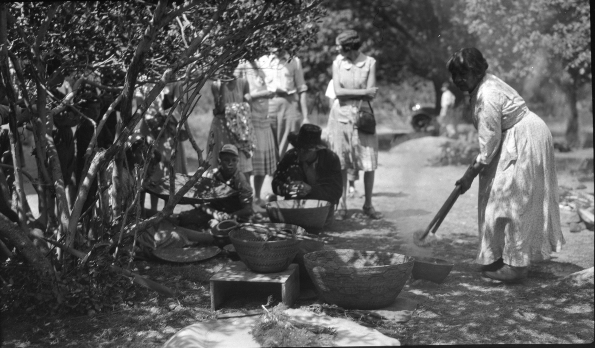 Maggie Howard Stone-boiling water for leaching basin behind museum with park visitors. Baskets from Yosemite Museum collection.