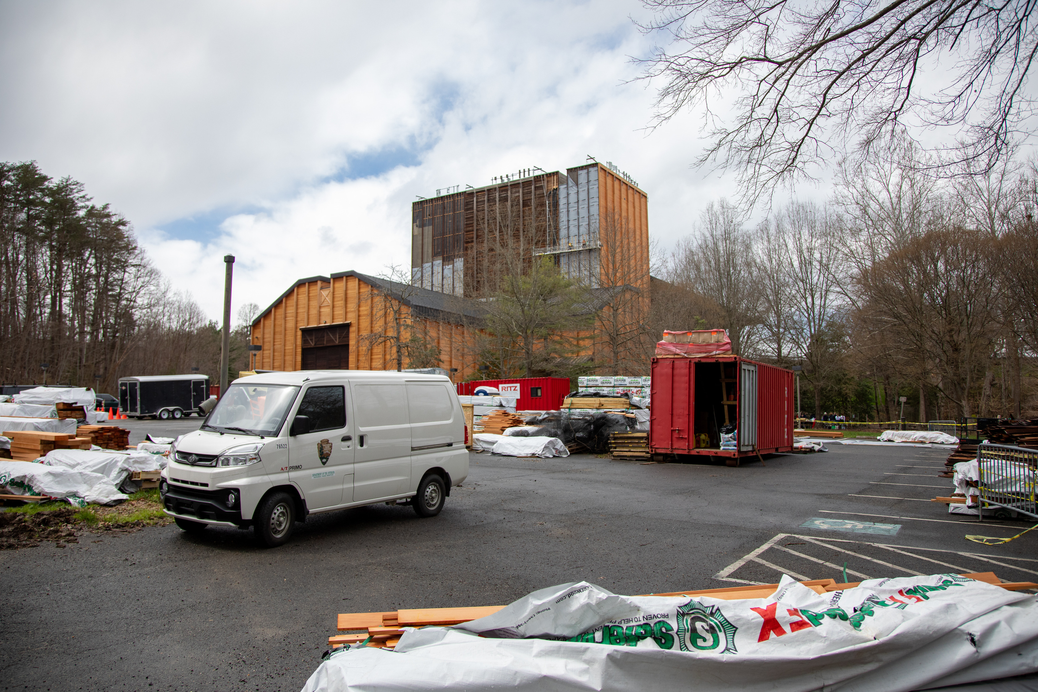 A white van is parked and surrounded by siding that is piled up on the ground. In the background, the entire back wall of the center is missing siding or still has old, dark brown siding.
