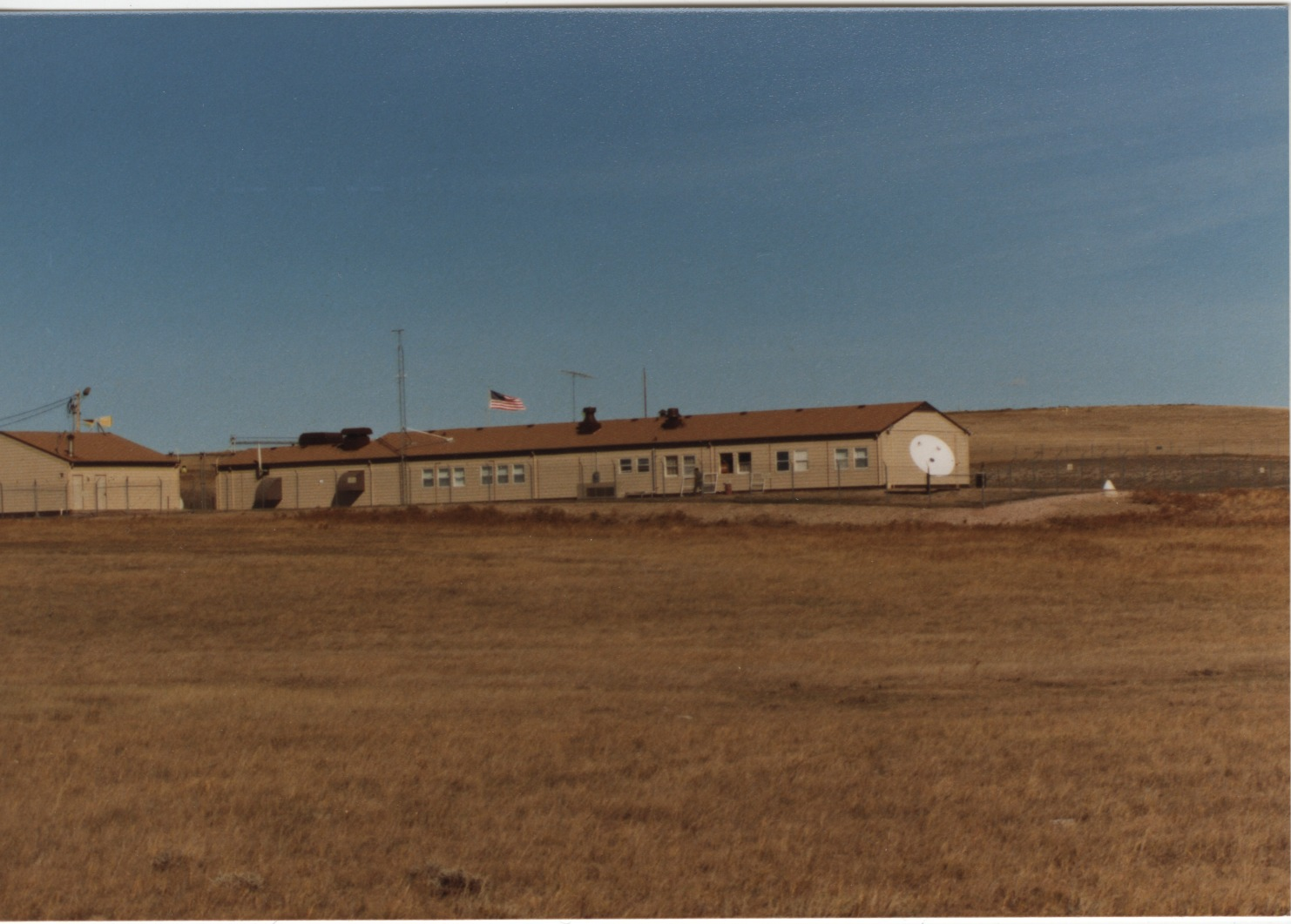 A long building inside a fenced compound in a prairie landscape