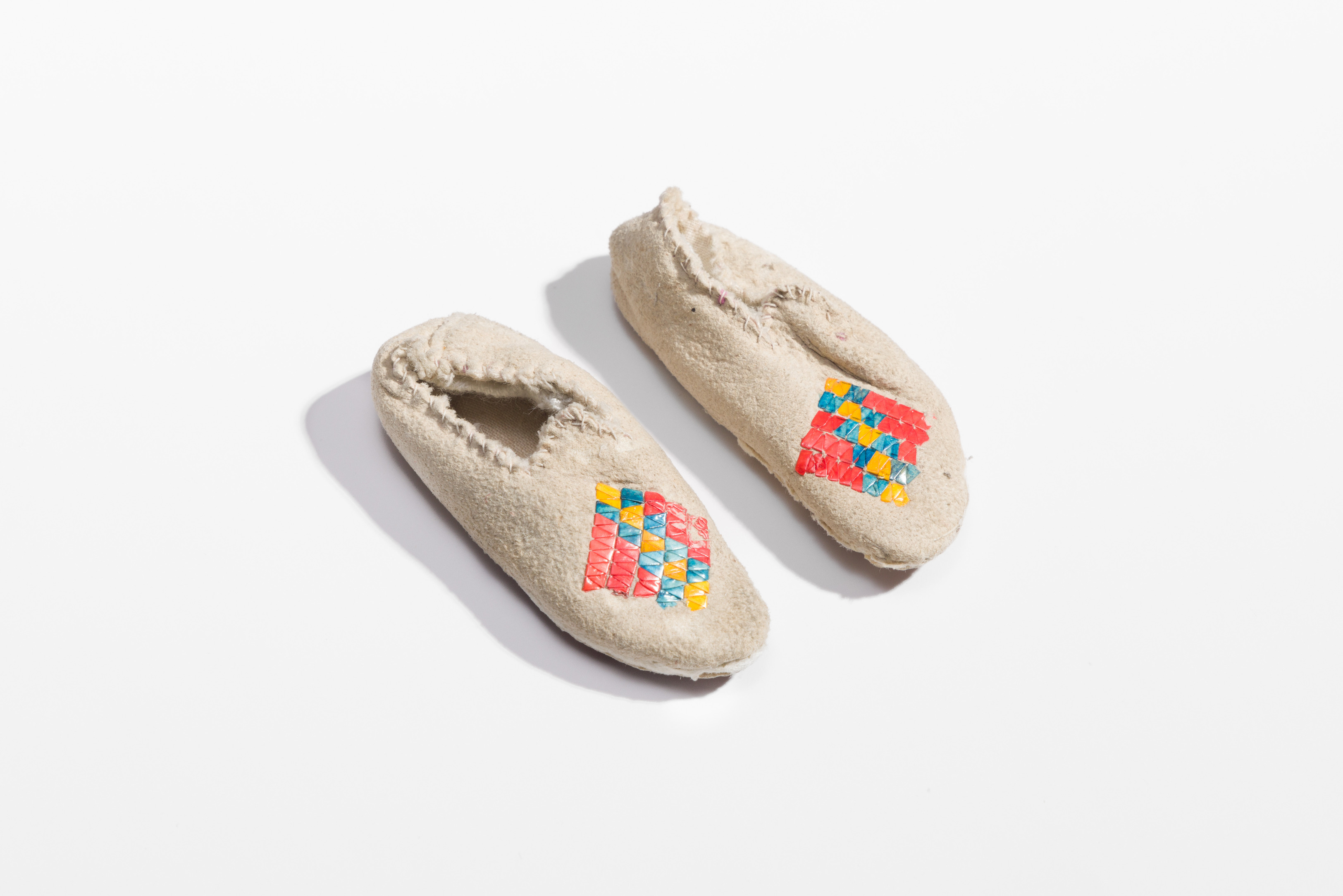 Very small moccasins with an orange, blue, and yellow diamond-shaped porcupine quill work on the toe