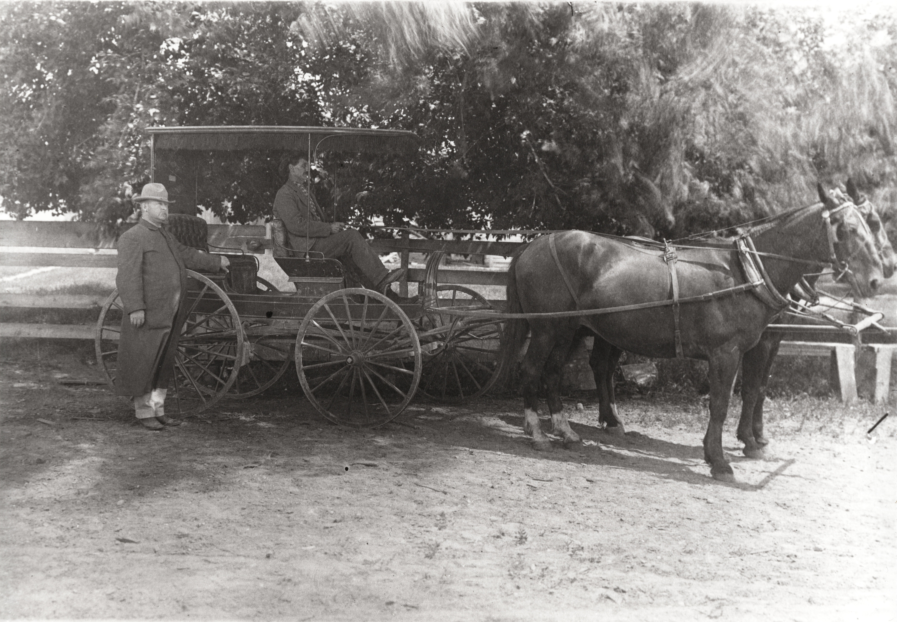 Black and white photograph of two men and a horse drawn buggy, one standing and one sitting in the buggy