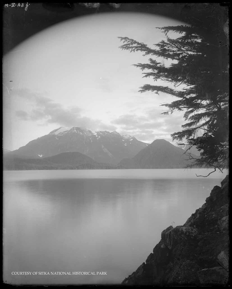 Rocky shoreline with ocean and distant mountains.