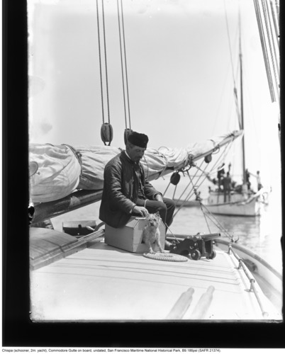 A man sitting on the deck of a schooner with a small dog in a little house next to a miniature cannon.